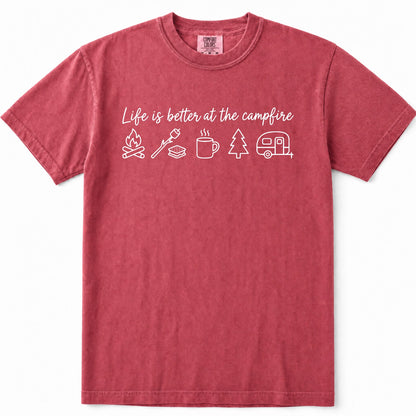 Crimson short-sleeve crewneck t-shirt in a washed, heathered red color, featuring a white graphic print on the chest that reads 'Life is better at the campfire' above simple white icons of a campfire, marshmallow, mug, pine tree, and camper trailer.