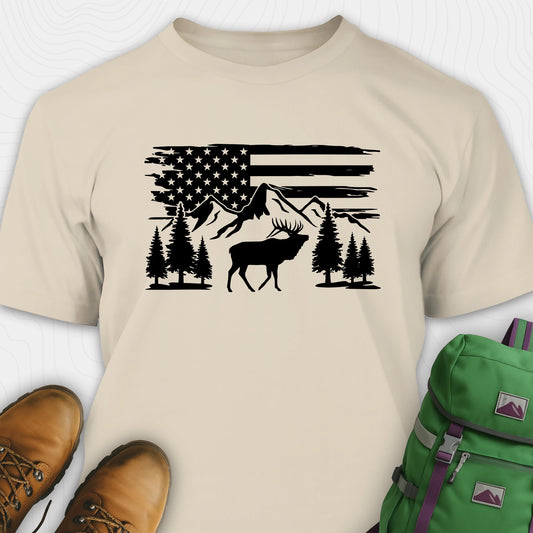 Beige deer t-shirt with black graphic design of an American flag, trees, and a moose, accompanied by brown boots and a green backpack.
