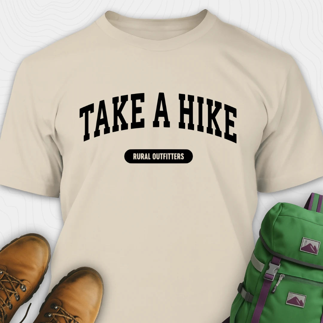 Beige t-shirt with 'Take a Hike' text, brown boots, and green backpack on a white background