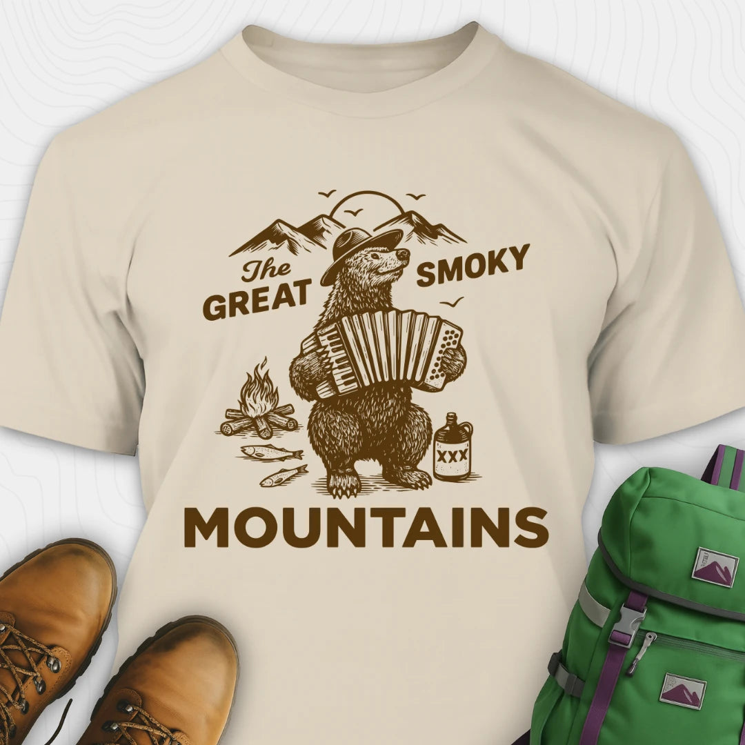 Beige t-shirt with bear playing an accordion graphic and 'The Great Smoky Mountains' text, paired with brown boots and a green backpack.