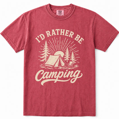 Crimson short-sleeve crewneck t-shirt in a washed, heathered red color, featuring a cream-colored graphic print on the front with the text 'I'D RATHER BE Camping' and an illustration of a tent, trees, and a sun.