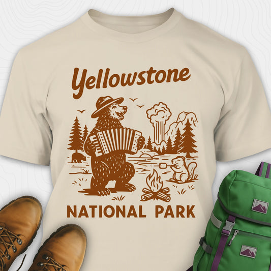 Sand t-shirt with a brown bear playing an accordion and “Yellowstone National Park” text, styled with hiking boots and a green backpack.
