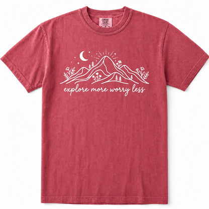 Crimson short-sleeve crewneck t-shirt in a washed, heathered red color, featuring a white graphic of mountains, a crescent moon, stars, and the text 'explore more worry less' printed across the chest.