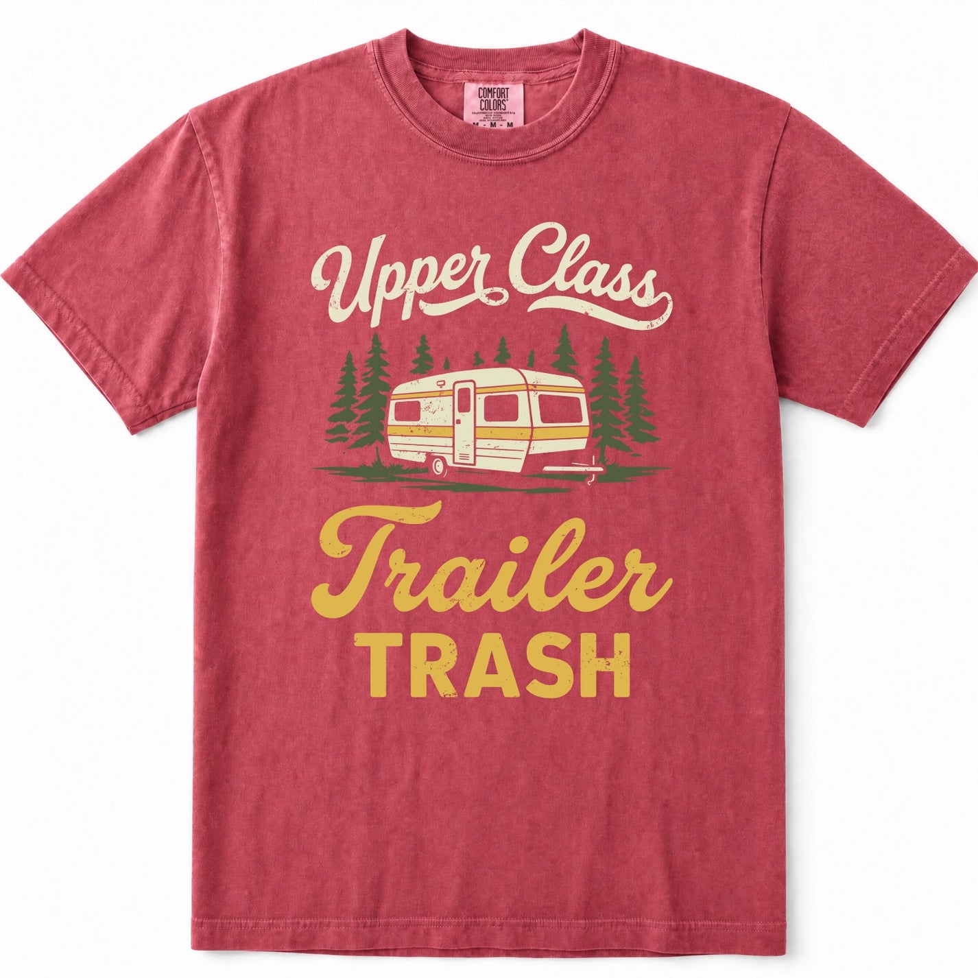 Crimson short-sleeve t-shirt with a vintage-style graphic that reads 'Upper Class Trailer TRASH' in cream and yellow lettering, featuring an illustration of a retro camper trailer and pine trees.