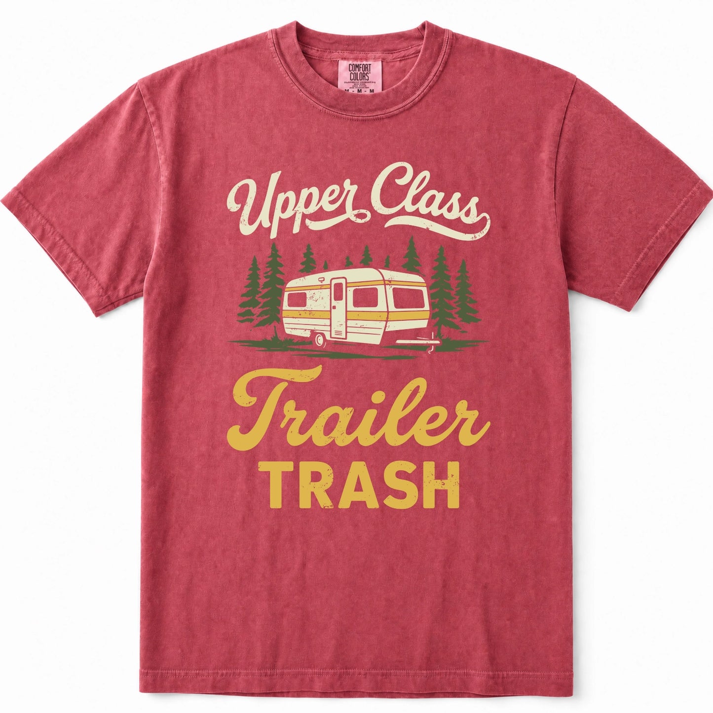 Crimson short-sleeve t-shirt with a vintage-style graphic that reads 'Upper Class Trailer TRASH' in cream and yellow lettering, featuring an illustration of a retro camper trailer and pine trees.