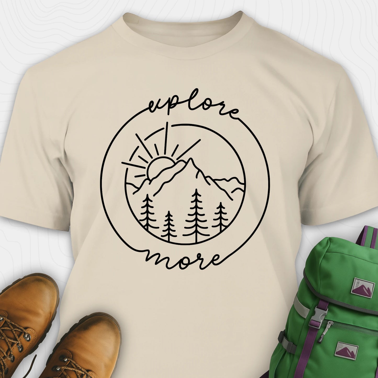 Sand explorer shirt with 'explore more' graphic design, brown boots, and green backpack on a white background