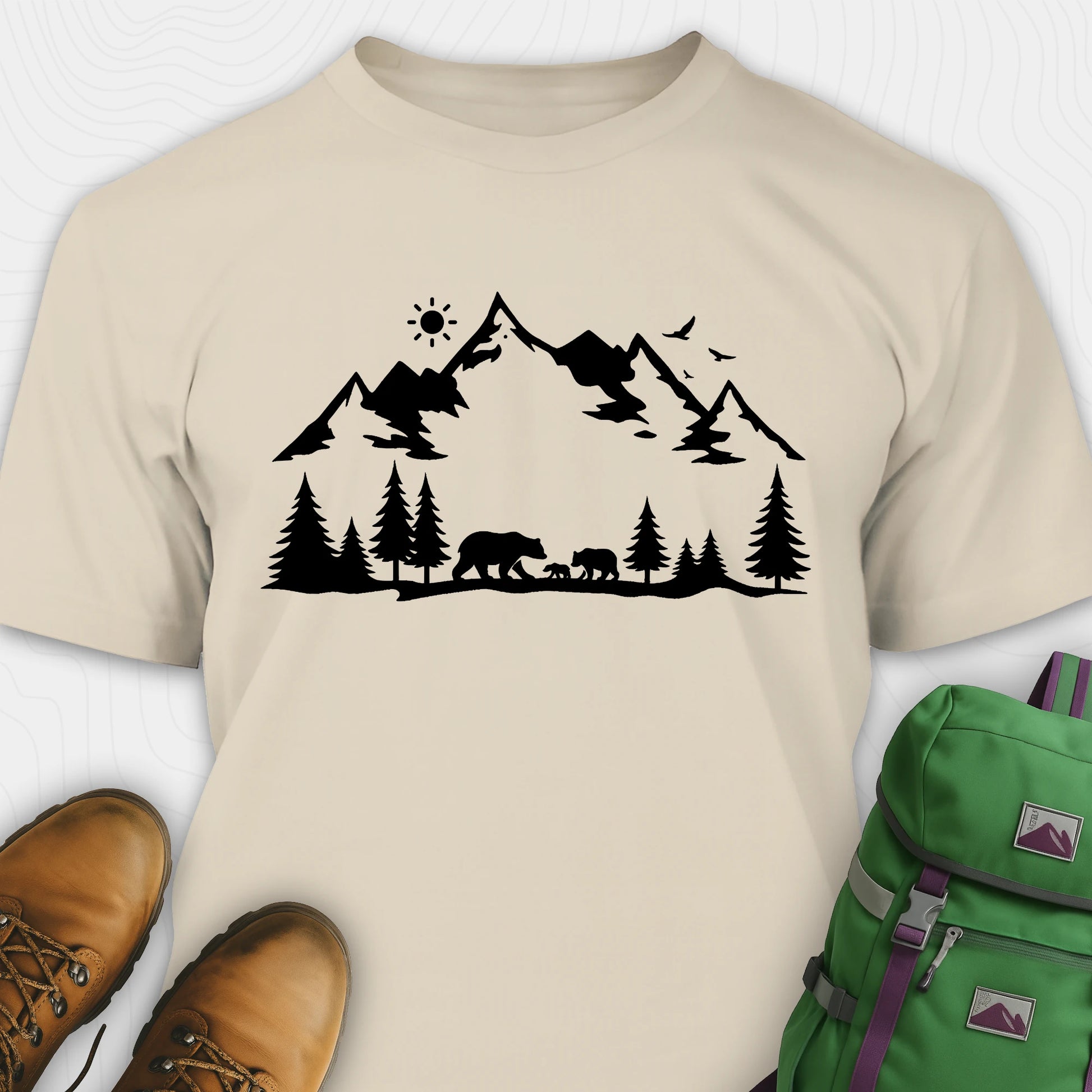 Natural wildlife t-shirt with black mountain and bear design, paired with brown boots and a green backpack on a white background.