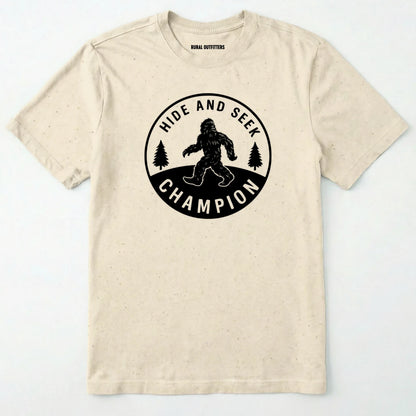 Natural bigfoot hide and seek champion shirt with forest emblem on a white background.