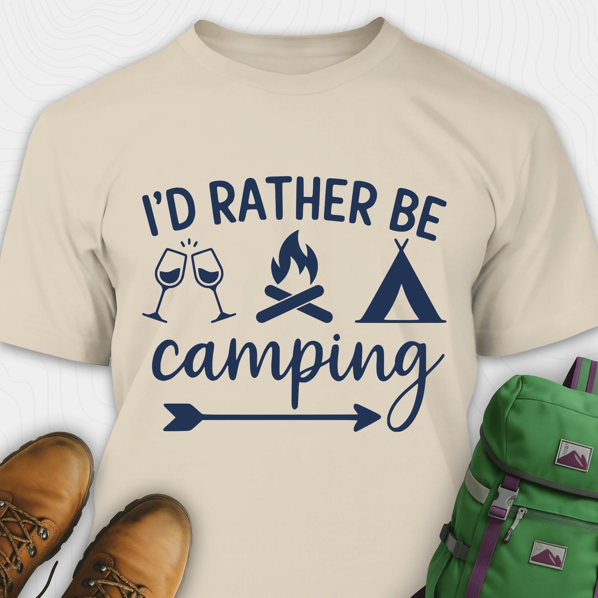 Sand women's camping shirt with 'I'd Rather Be Camping' text and camping icons, paired with hiking boots and a green backpack.