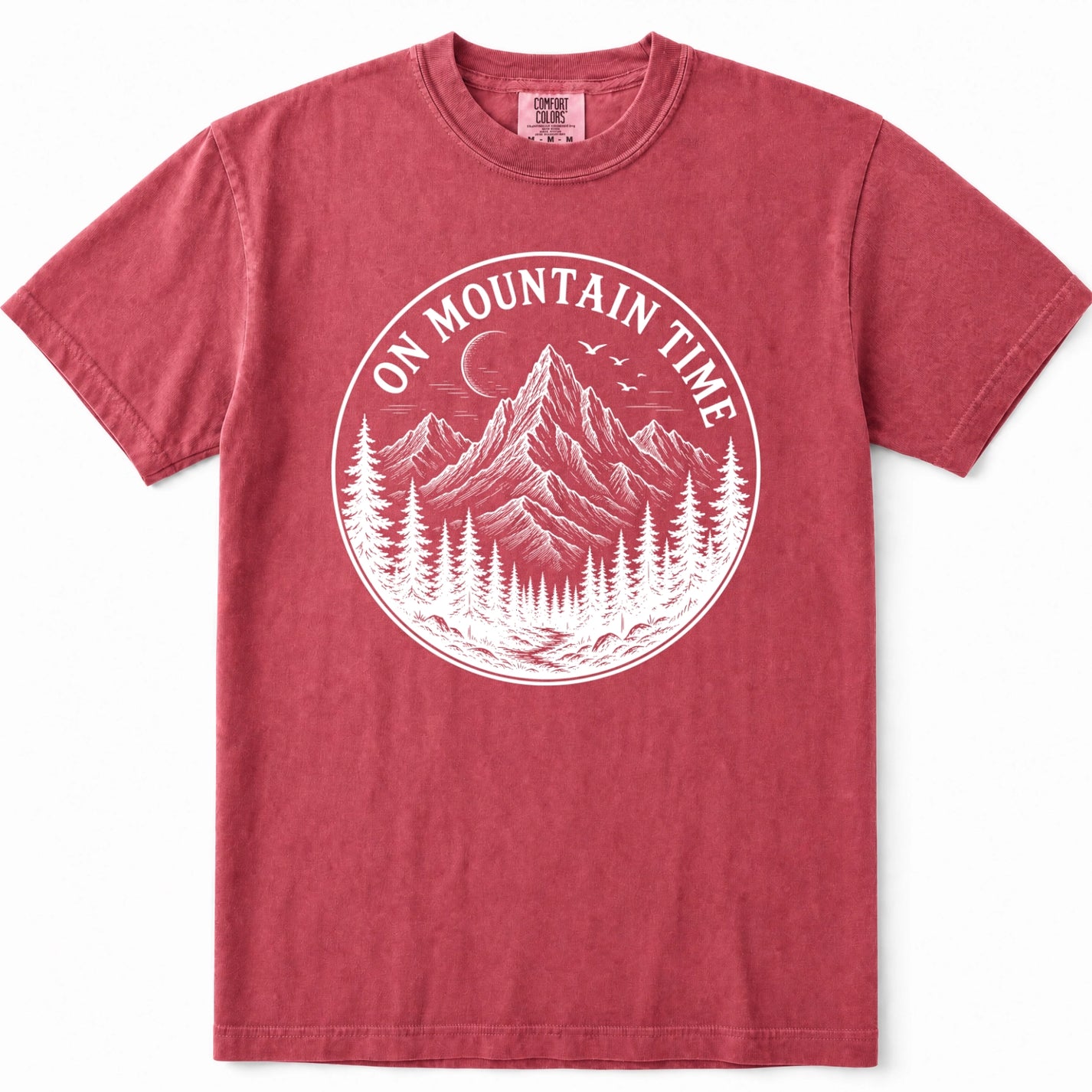 Crimson short-sleeve crewneck t-shirt in a washed, heathered red color, featuring a white circular graphic on the chest with the text 'ON MOUNTAIN TIME' and an illustration of a mountain, pine trees, and a crescent moon.