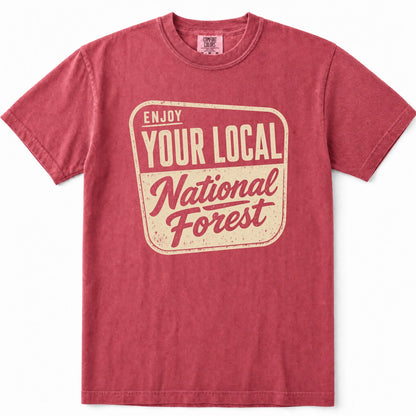 Crimson short-sleeve crewneck t-shirt in a washed, heathered red color, featuring a distressed cream-colored graphic on the front that reads 'ENJOY YOUR LOCAL National Forest'.