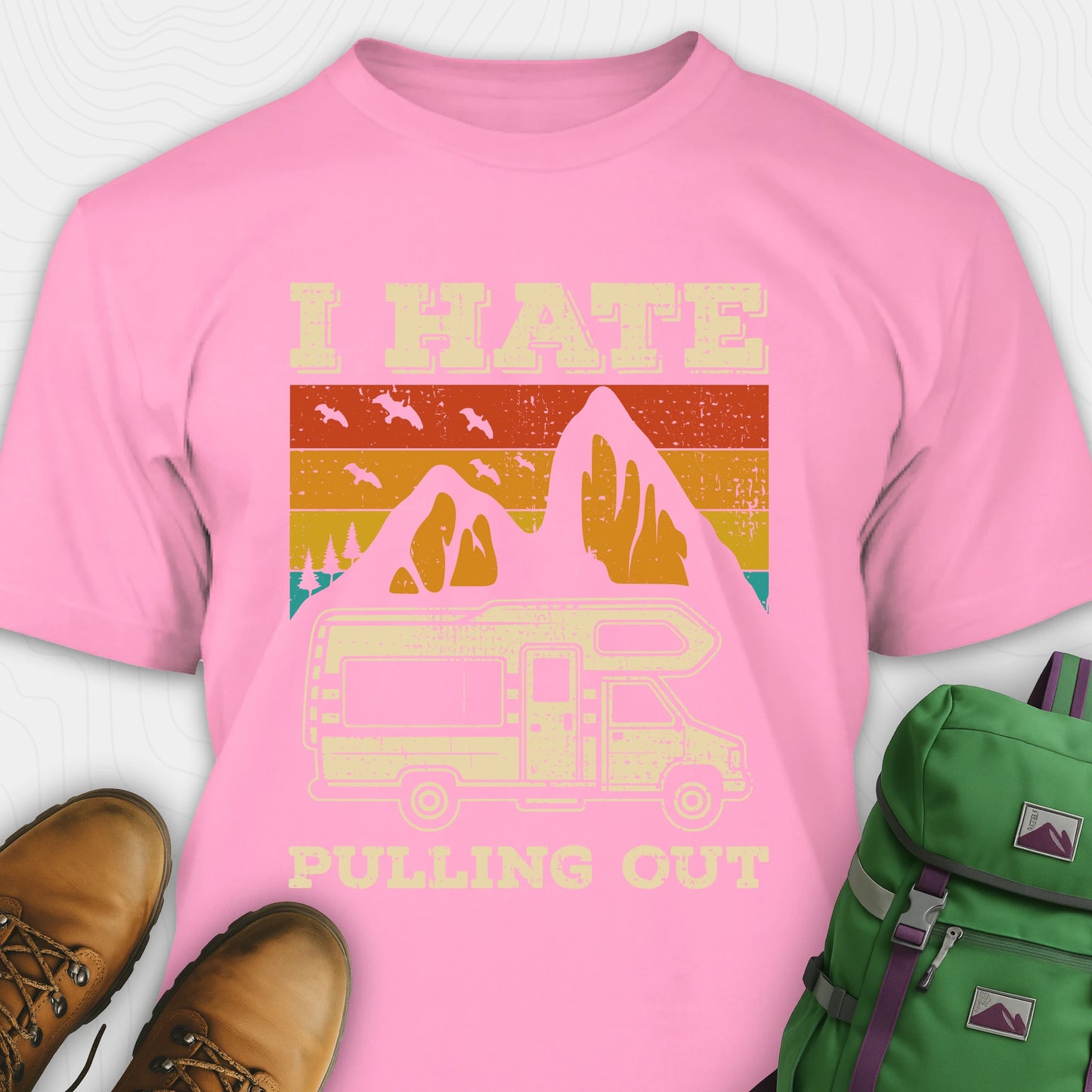 Pink I hate pulling out shirt with a graphic design of an RV and mountains, displayed with brown boots and a green backpack.