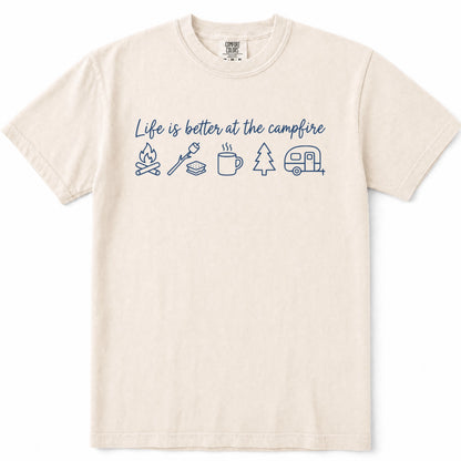 Ivory cream-colored short-sleeve t-shirt with a blue graphic on the chest that reads 'Life is better at the campfire' above simple line drawings of a campfire, marshmallow, mug, pine tree, and camper trailer.
