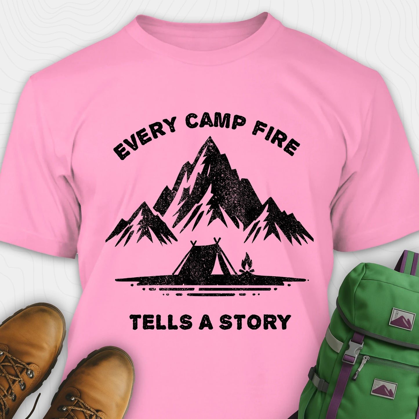 Pink campfire story shirt with mountains and tent graphic and "every camp fire tells a story" text