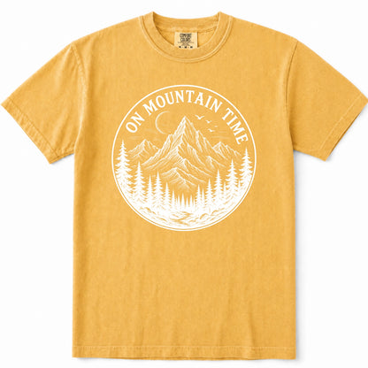 Mustard yellow short-sleeve t-shirt with a white circular graphic on the chest depicting a mountain, pine trees, and the text 'ON MOUNTAIN TIME'.