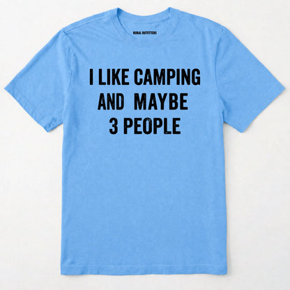 Carolina Blue short-sleeve t-shirt with bold black text reading 'I LIKE CAMPING AND MAYBE 3 PEOPLE' across the chest, laid flat against a light off-white background.