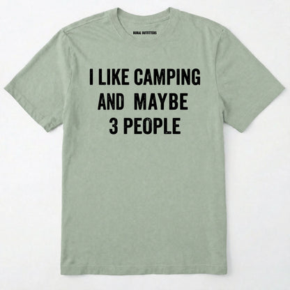 Sage short-sleeve t-shirt with bold white text reading 'I LIKE CAMPING AND MAYBE 3 PEOPLE' across the chest, laid flat against a light off-white background.