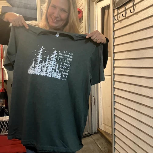 Person holding a dark green t-shirt with a graphic design and text.