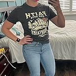 Person wearing a black t-shirt with text and graphics, standing in a bedroom.