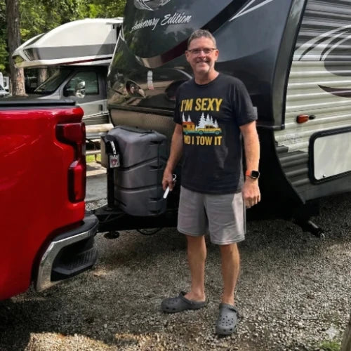 Man standing next to a red truck with an open trailer, wearing a humorous t-shirt.