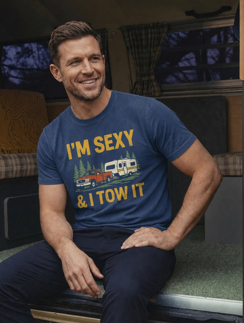 Man wearing a Rural Outfitters outdoor shirt with 'I'm Sexy and I Tow It' text and graphic inside a vehicle.
