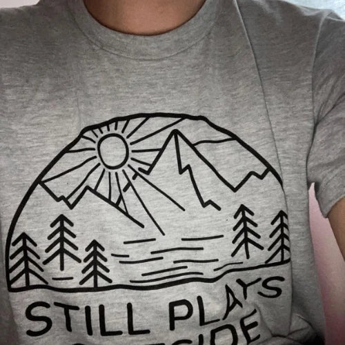 Gray t-shirt with a mountain and sun design and text on a plain background