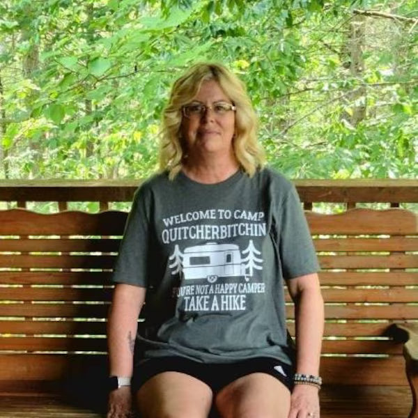Woman wearing a t-shirt with a humorous message, sitting on a wooden bench outdoors.